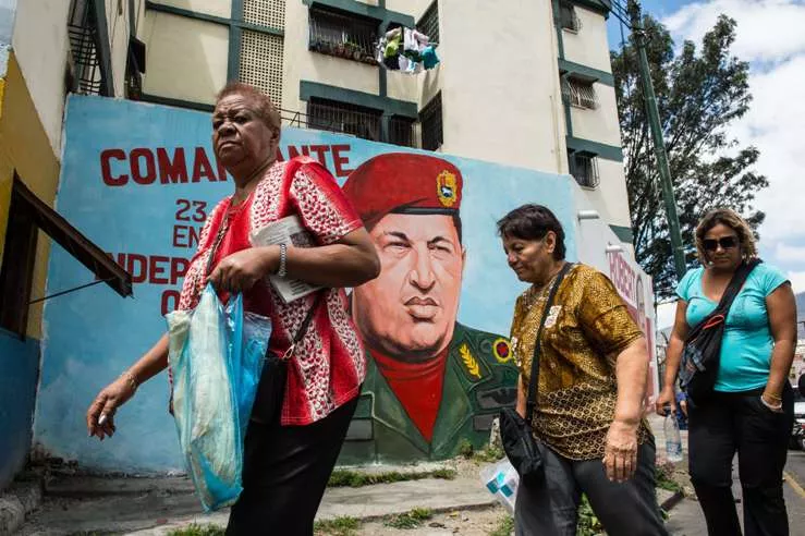 People walk by a mural painting depicting late Venezuelan President Hugo Chavez at 23 de Enero community in Caracas on February 27, 2015. Next March 5, marks the second anniversary of Chavez’s death. The eternal proclaimed commander who directed the South American nation for more than a decade has left a void that neither his political heirs, nor opponents have been able to fill. AFP PHOTO/FEDERICO PARRA