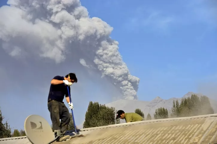 Men clan the roof of a house in La Ensenada, Chile with the Calbuco volcano in the background, on April 24, 2015. Southern Chile remained on alert Friday for another eruption from the Calbuco volcano after it burst into life in spectacular, fiery fashion for the first time in half a century, forcing 5,000 people to evacuate and lighting up the night sky. AFP PHOTO/MARTIN BERNETTI