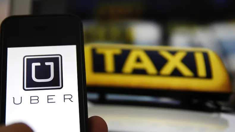 File illustration picture showing the logo of car-sharing service app Uber on a smartphone next to the picture of an official German taxi sign