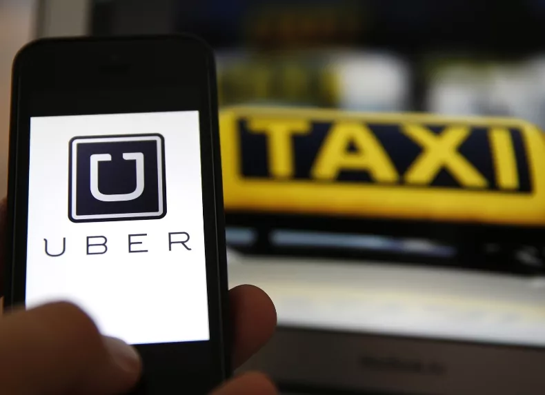 File illustration picture showing the logo of car-sharing service app Uber on a smartphone next to the picture of an official German taxi sign