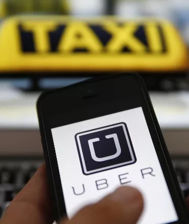 An illustration picture shows the logo of car-sharing service app Uber on a smartphone next to the picture of an official German taxi sign