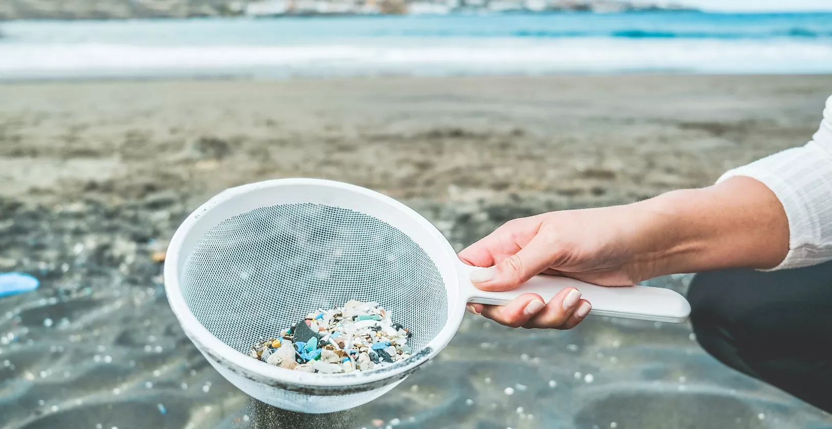 Young woman cleaning microplastics from sand on the beach – Environmental problem, pollution and ecolosystem warning concept – Focus on hand