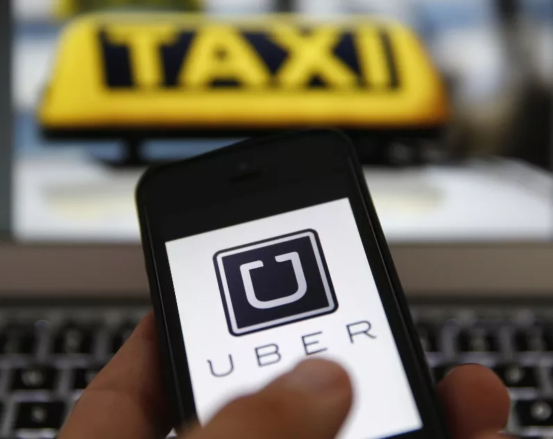 An illustration picture shows the logo of car-sharing service app Uber on a smartphone next to the picture of an official German taxi sign