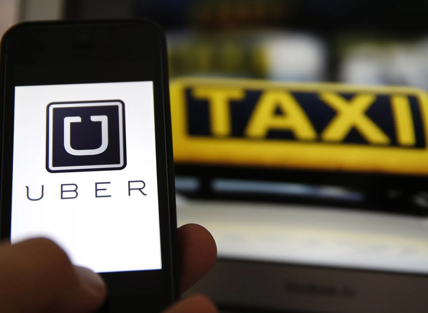 File illustration picture showing the logo of car-sharing service app Uber on a smartphone next to the picture of an official German taxi sign