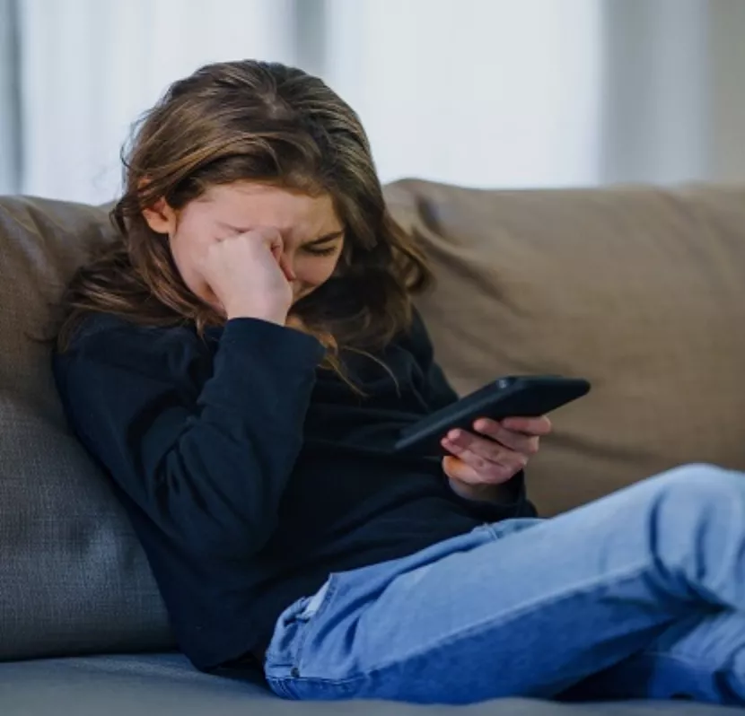 Small girl with smartphone sitting indoors on sofa, crying.