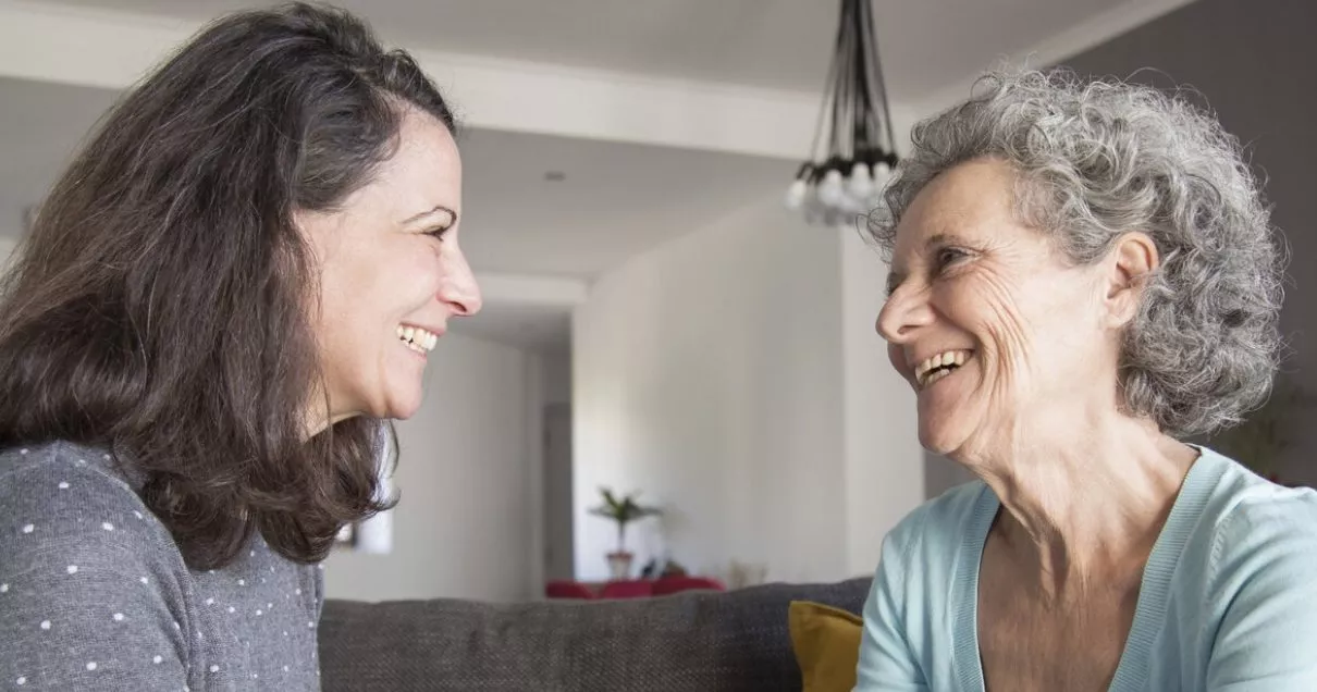 Elderly woman and her daughter laughing and holding hands