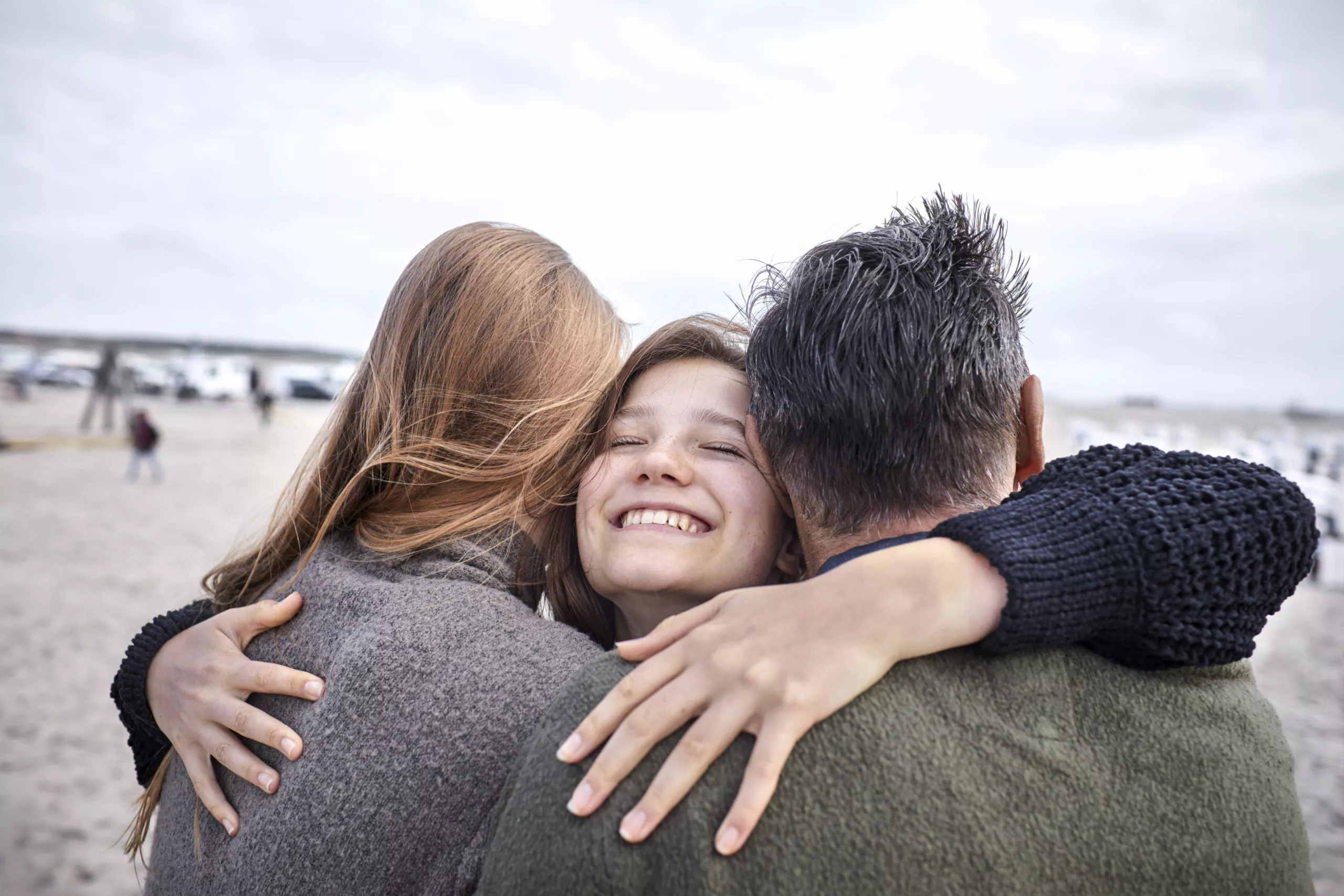 Happy girl hugging woman and man on the beach