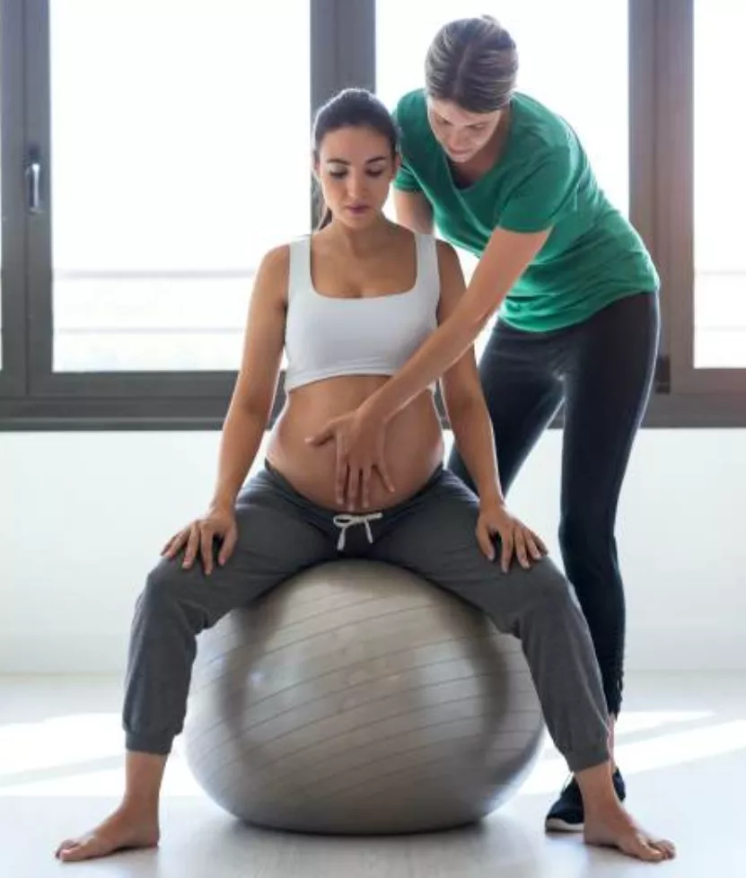 Physiotherapist helping to beautiful pregnant woman for doing pi