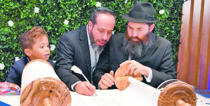 David Kreh escribiendo en la Torá junto al rabino Shimon Selman. Observa el  niño Eitan.