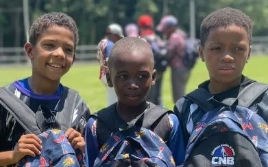 Niños muestran las mochilas que les donó el Comisionado.