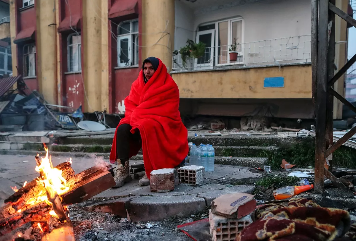 People warm up near collapsed buildings following a major earthquake in Hatay