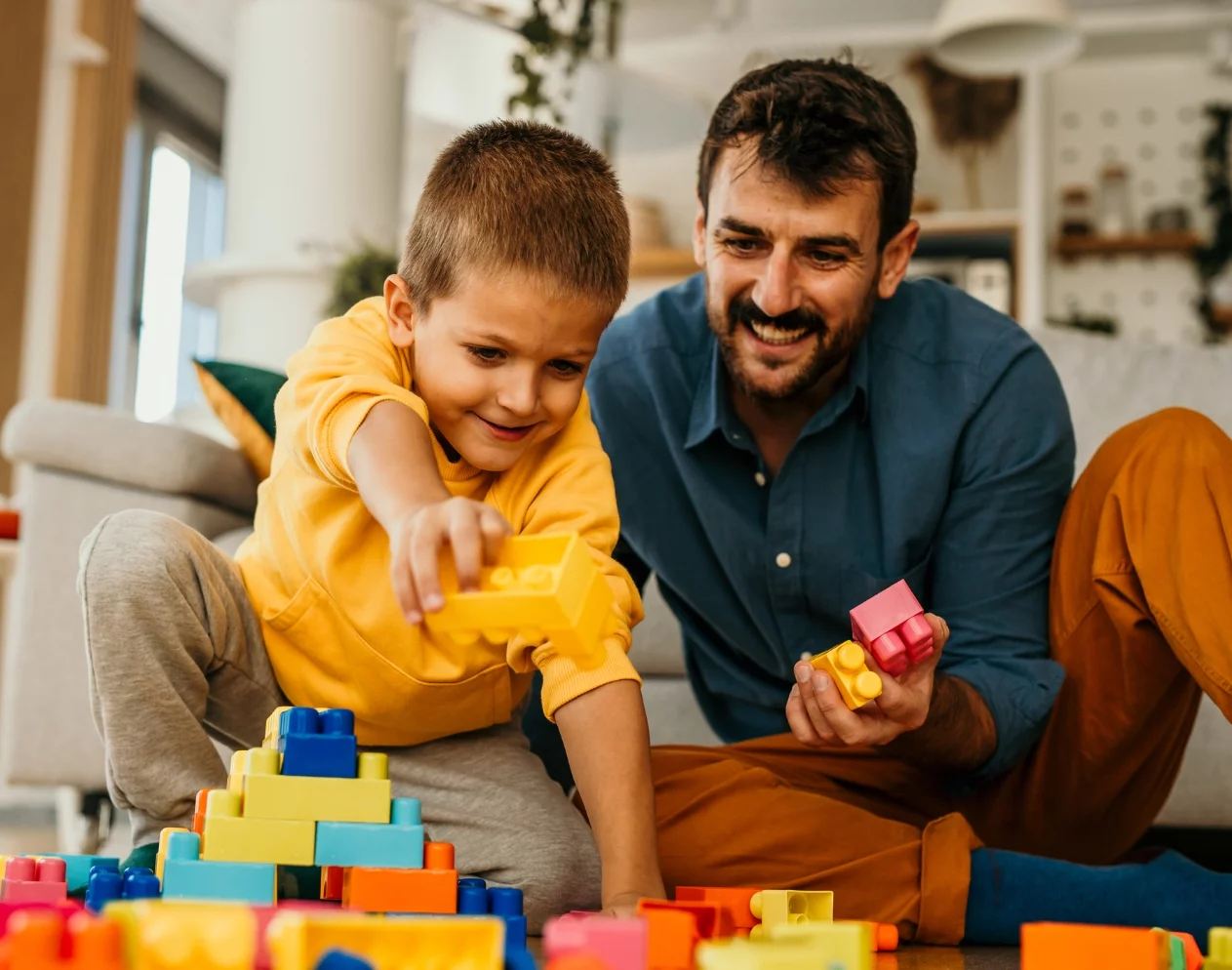 Father and his son playing with cubes on the floor in the living room.