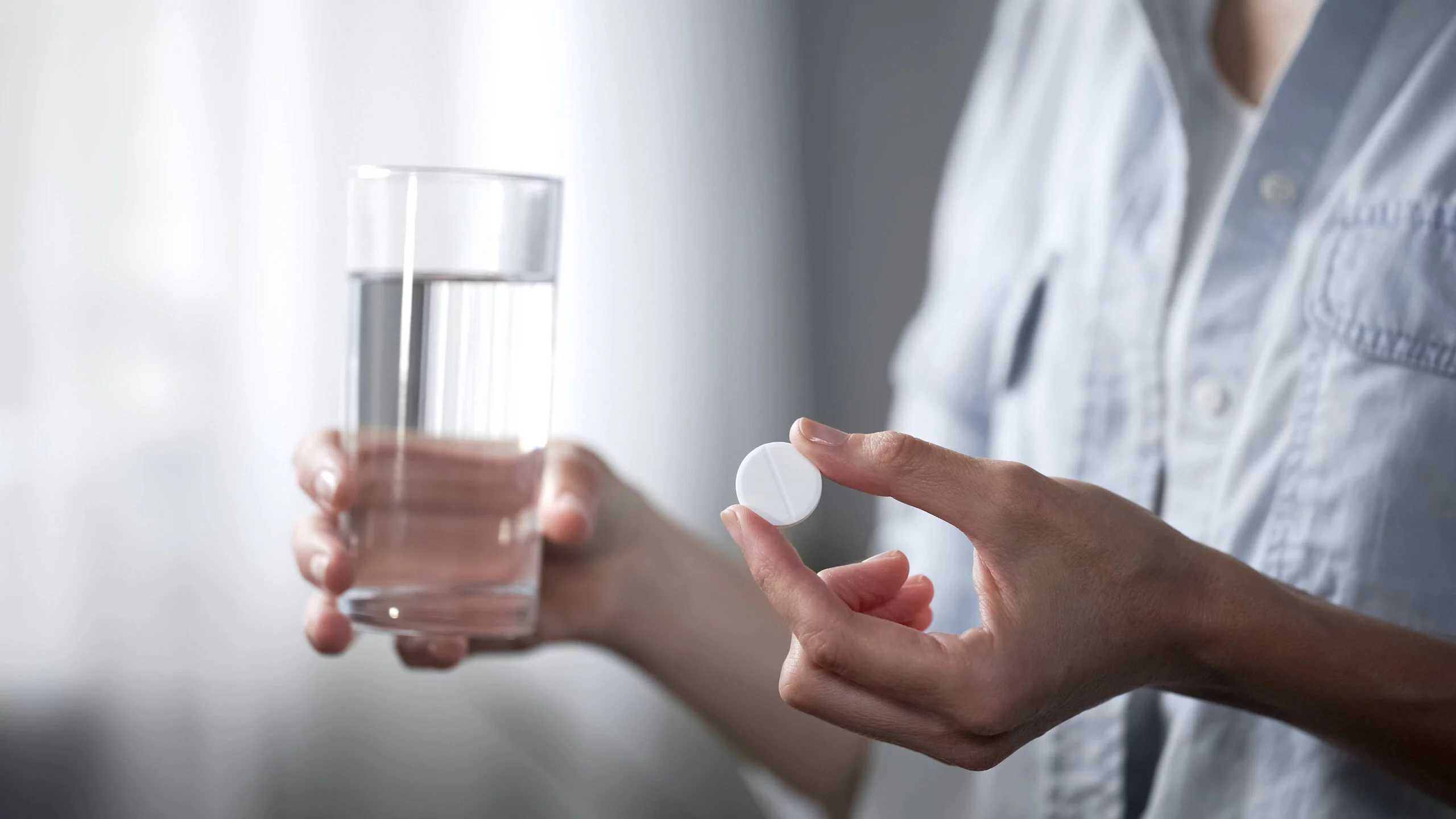 Female hand holding pill and water glass in hands, medicine and healthcare