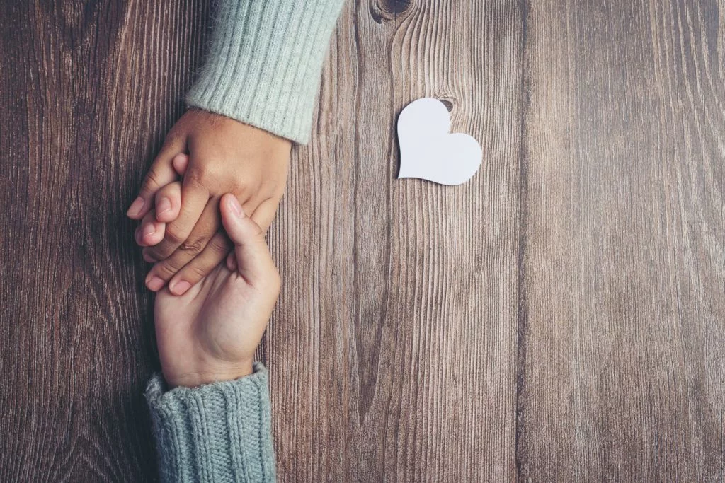 dos-personas-cogidas-mano-amor-calidez-mesa-madera-2-1-1024×683