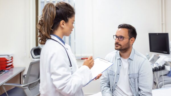 Serious man consulting with young female physician doctor at checkup meeting in hospital. Skilled general practitioner giving healthcare medical advices to patient.